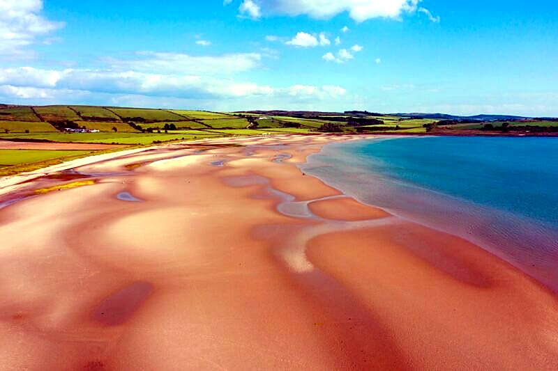 Aerial view of Ettrick Bay on the Isle of Bute, with wide sandy flats, shallow pools and green farmland rolling down to the shore