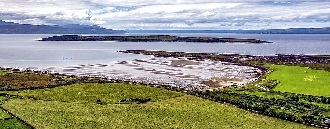 Aerial view of St Ninian's Bay on the Isle of Bute, with tidal sands, green pasture and the mainland hills across the water